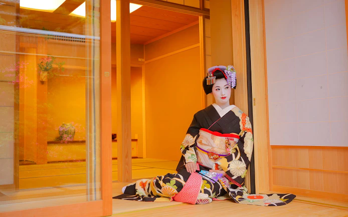 Geisha in traditional kimono posing in a Japanese tea house.