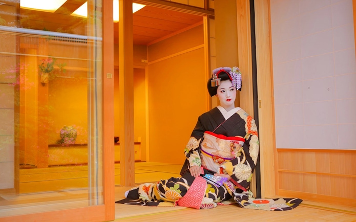 Geisha in traditional kimono posing in a Japanese tea house.