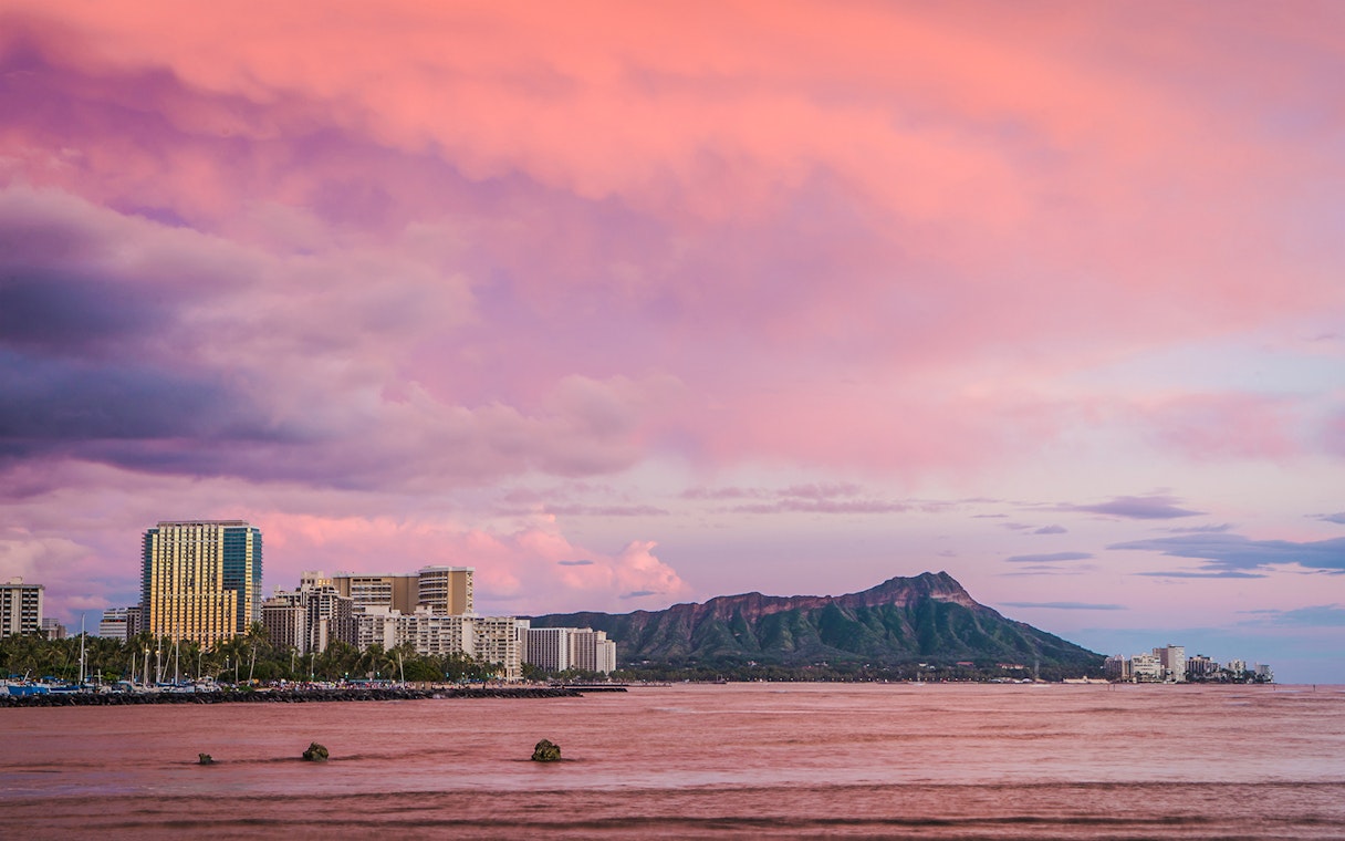 Diamond Head volcano and Honolulu skyline viewed from the ocean at sunset.
