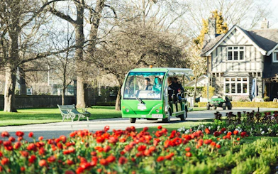 Tour tram in Christchurch Botanic Gardens with blooming flowers and historic building.