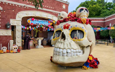 Giant skull decoration at PortAventura Park Halloween event with colorful banners and festive decor.