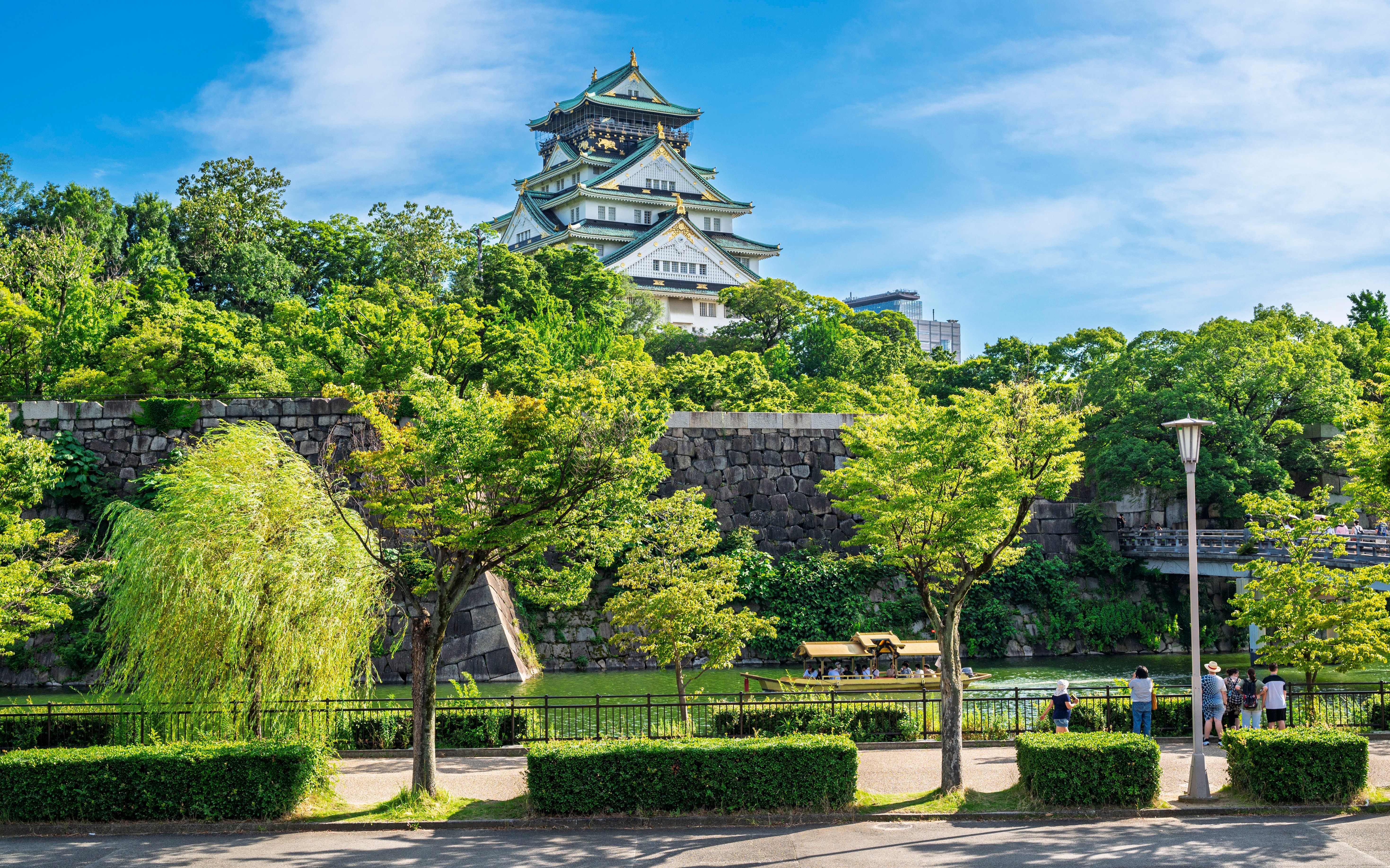 Osaka Castle surrounded by lush greenery and a stone wall in Osaka, Japan.