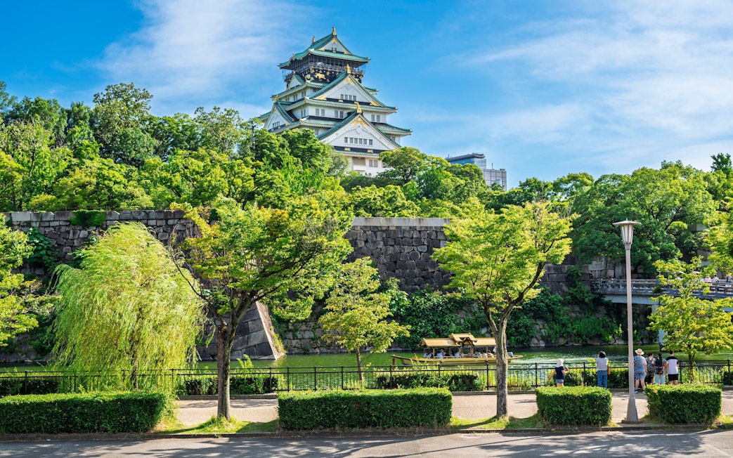 Osaka Castle surrounded by lush greenery and a stone wall in Osaka, Japan.