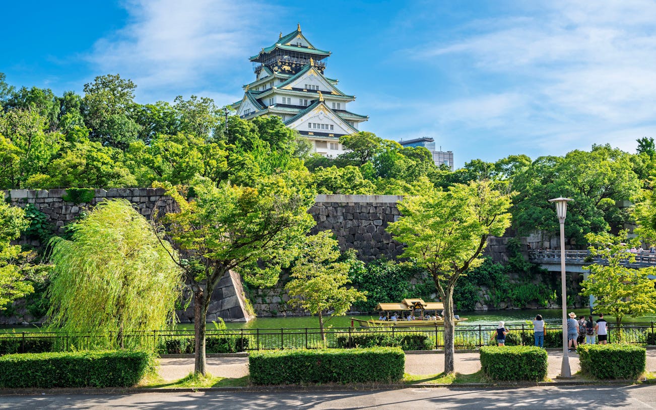 Osaka Castle surrounded by lush greenery and a stone wall in Osaka, Japan.