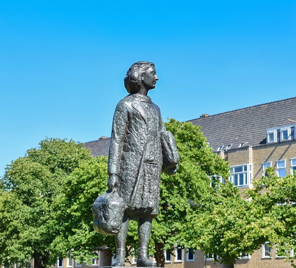 Anne Frank statue in Amsterdam with trees and buildings in the background.