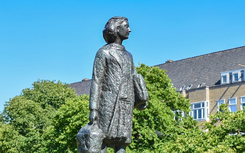 Anne Frank statue in Amsterdam with trees and buildings in the background.