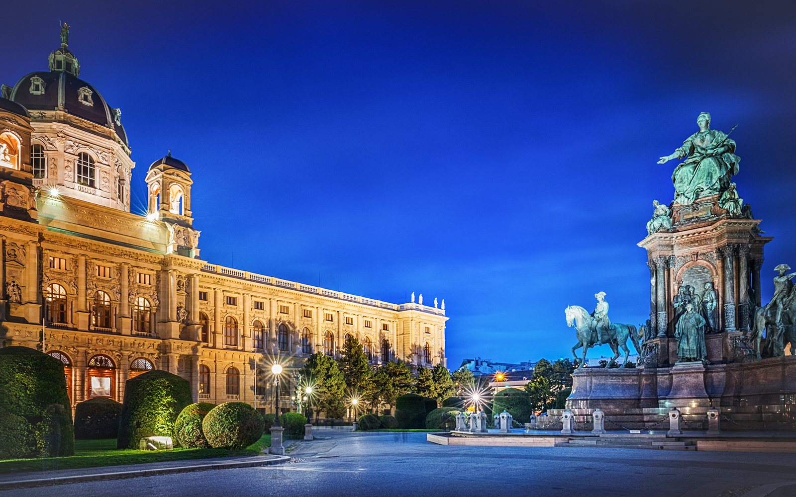 Maria Theresia Monument illuminated at night in Vienna, Austria, with surrounding architecture.