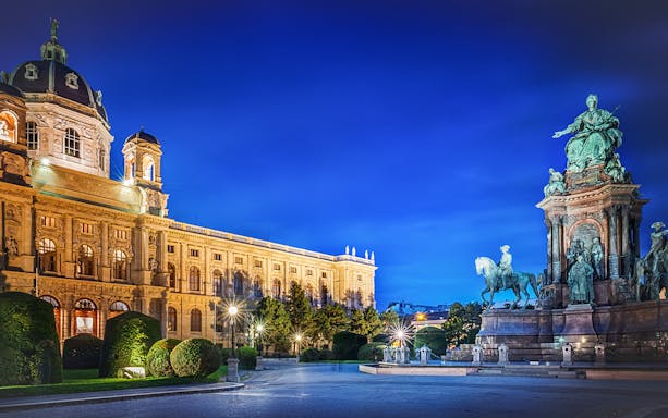Maria Theresia Monument illuminated at night in Vienna, Austria, with surrounding architecture.