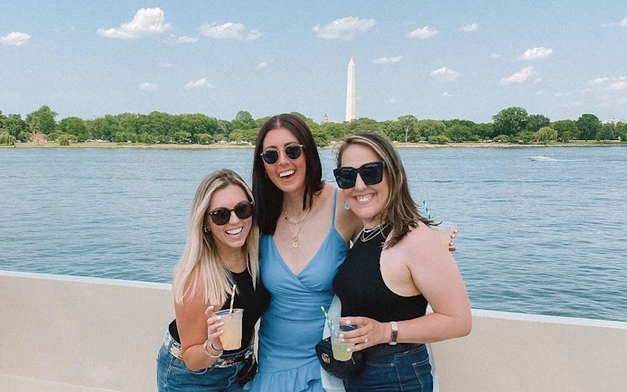 Three people enjoying drinks on a yacht with Washington Monument in the background, Washington, DC.