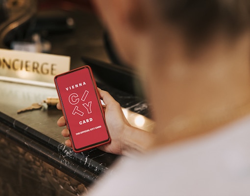 Person holding a phone displaying Vienna City Card at a concierge desk.