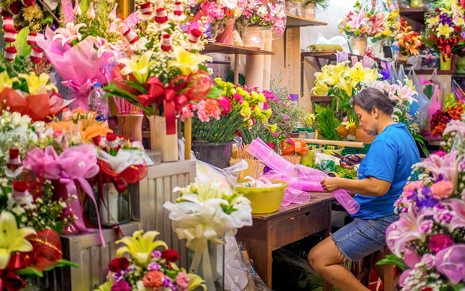 Florist arranging flowers at a vibrant Bangkok market during night bike tour.