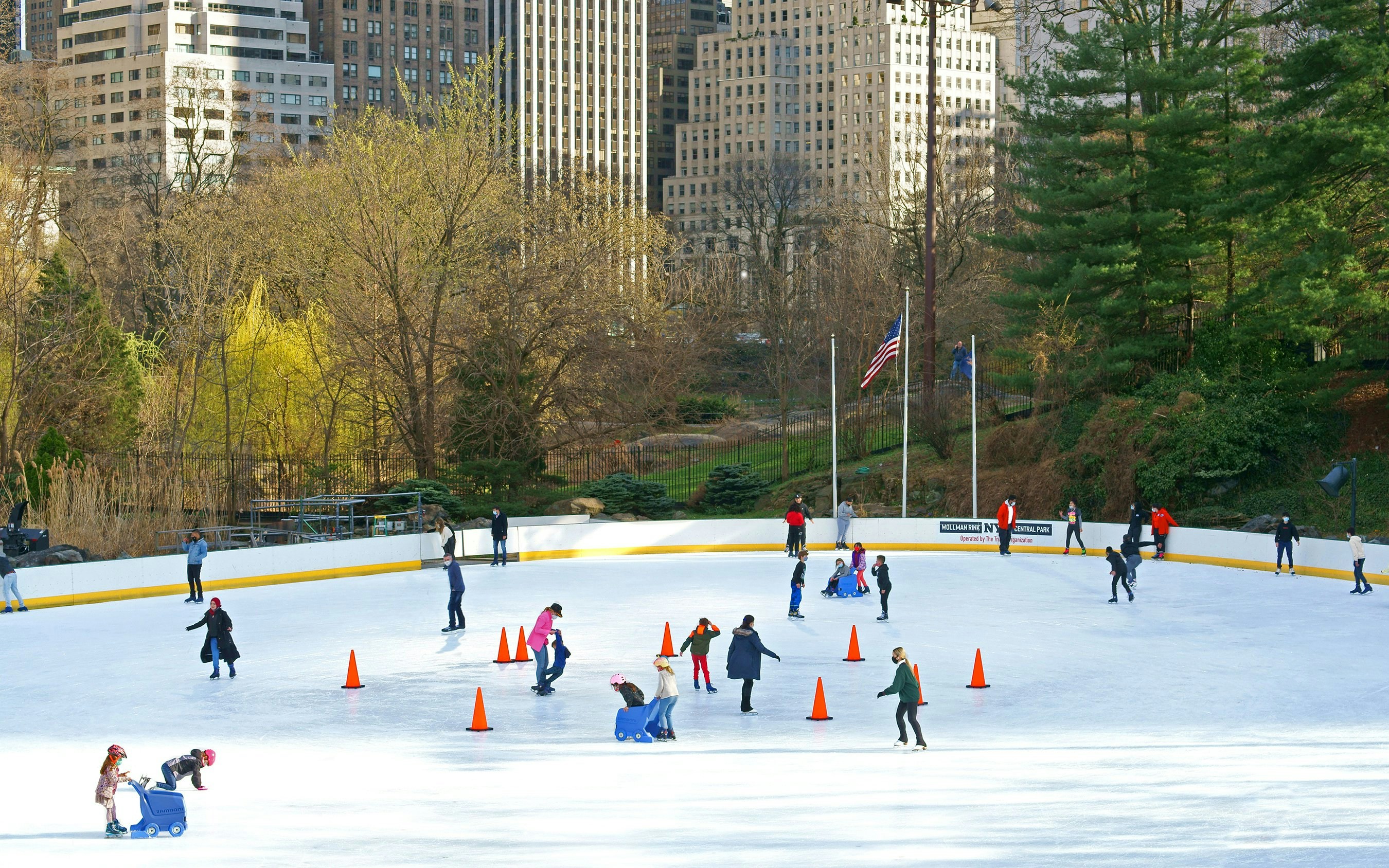 Ice skaters at Wollman Rink in Central Park, New York, with city buildings in the background.