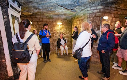Group listening to a guide in the Paris Catacombs during a tour.