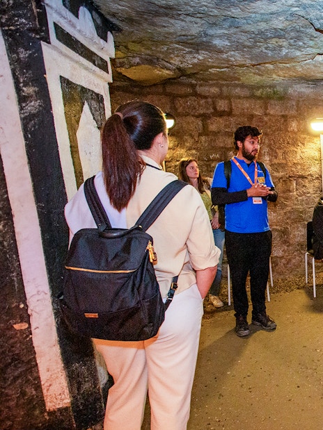 Group listening to a guide in the Paris Catacombs during a tour.