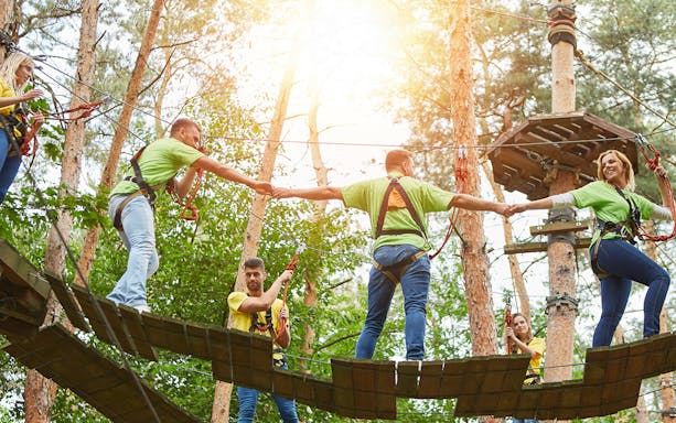 People on a treetop adventure course at Montes de Laboreiro, connected by safety harnesses.