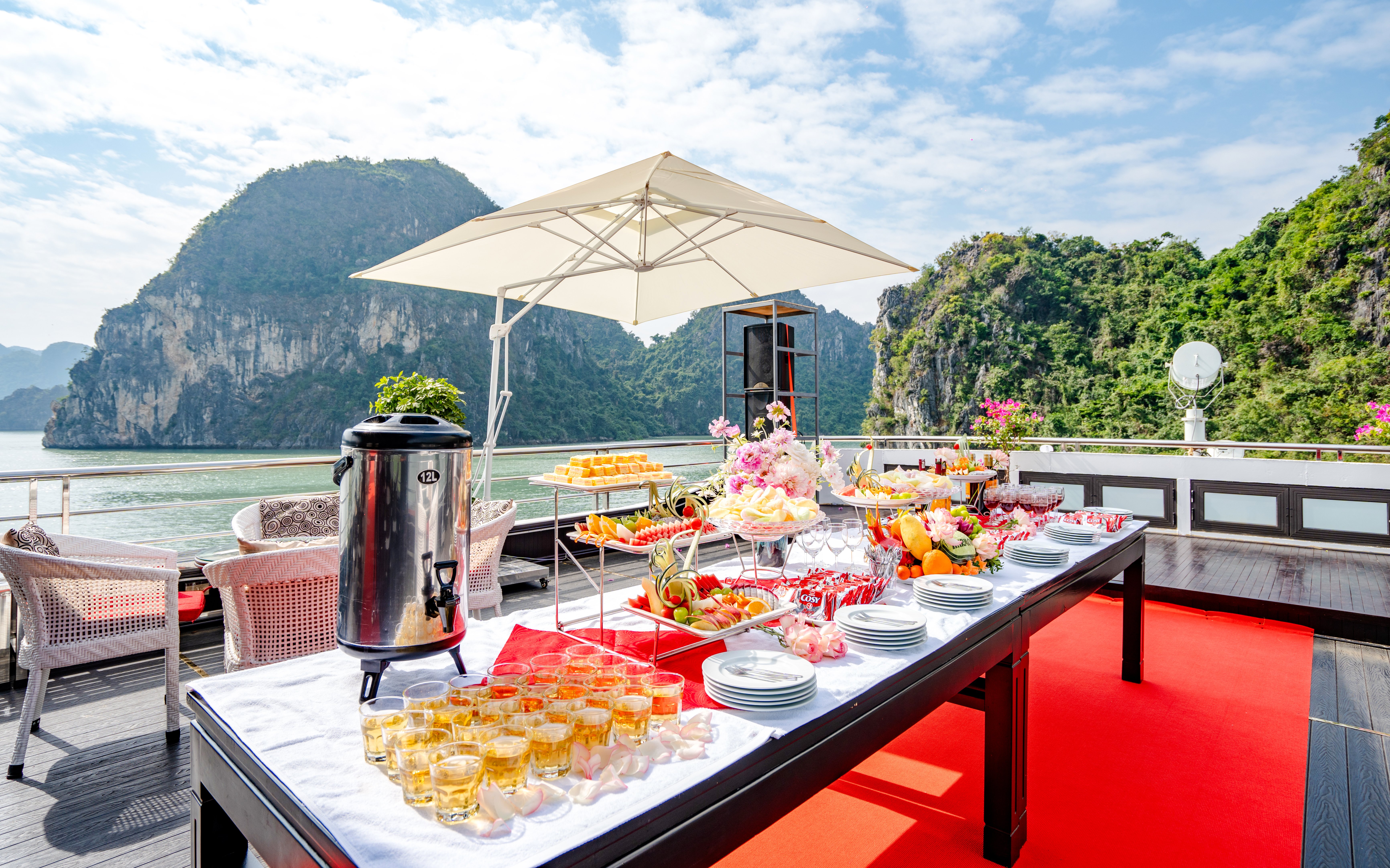 Refreshments setup on Phong Hai Harmony Cruise deck with scenic limestone cliffs in the background.