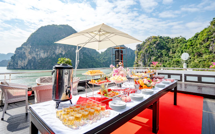 Refreshments setup on Phong Hai Harmony Cruise deck with scenic limestone cliffs in the background.