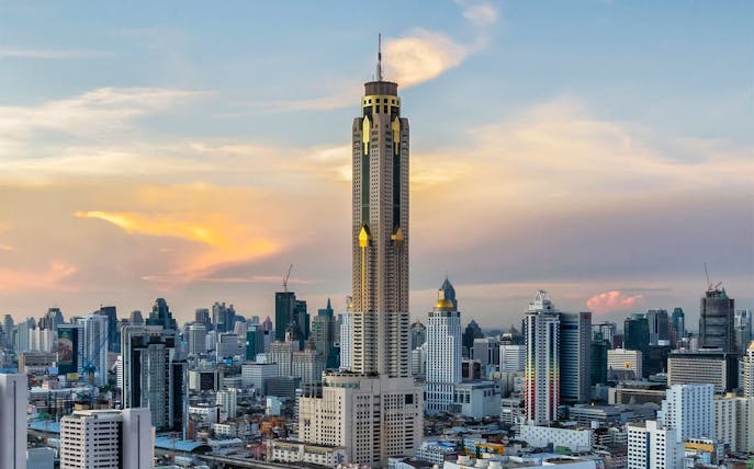 Baiyoke Sky Hotel towering over Bangkok skyline at sunset.