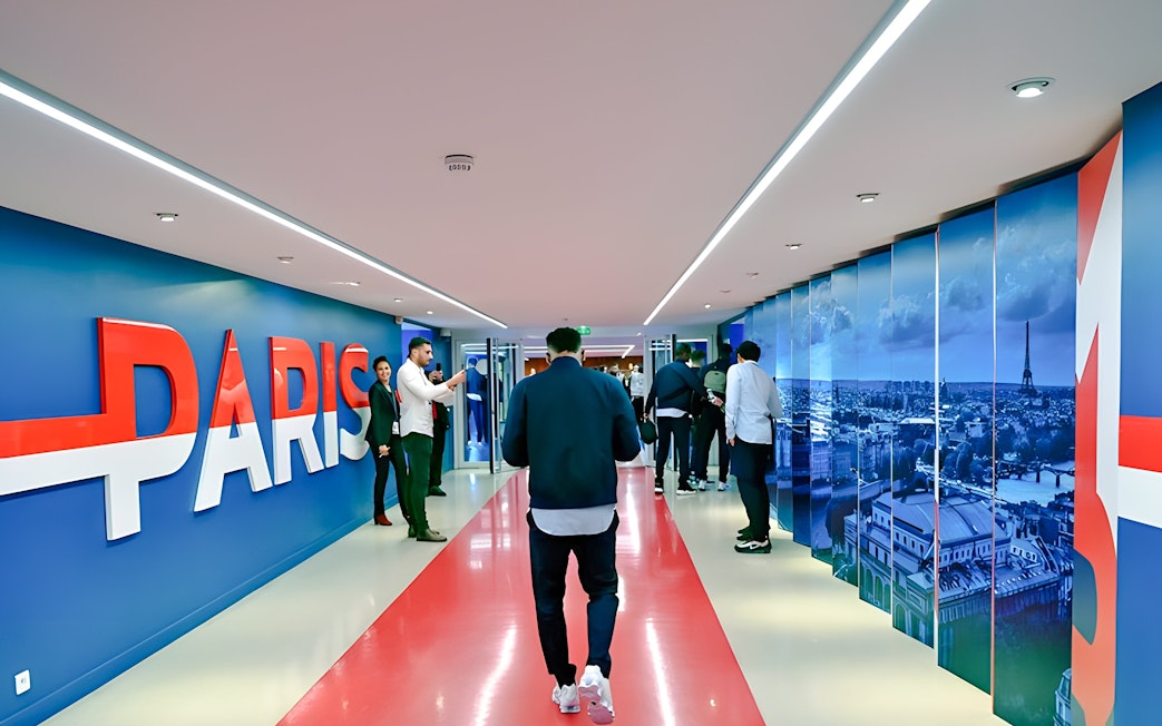 Hallway inside PSG Stadium, Paris, with people walking and large "Paris" sign on the wall.