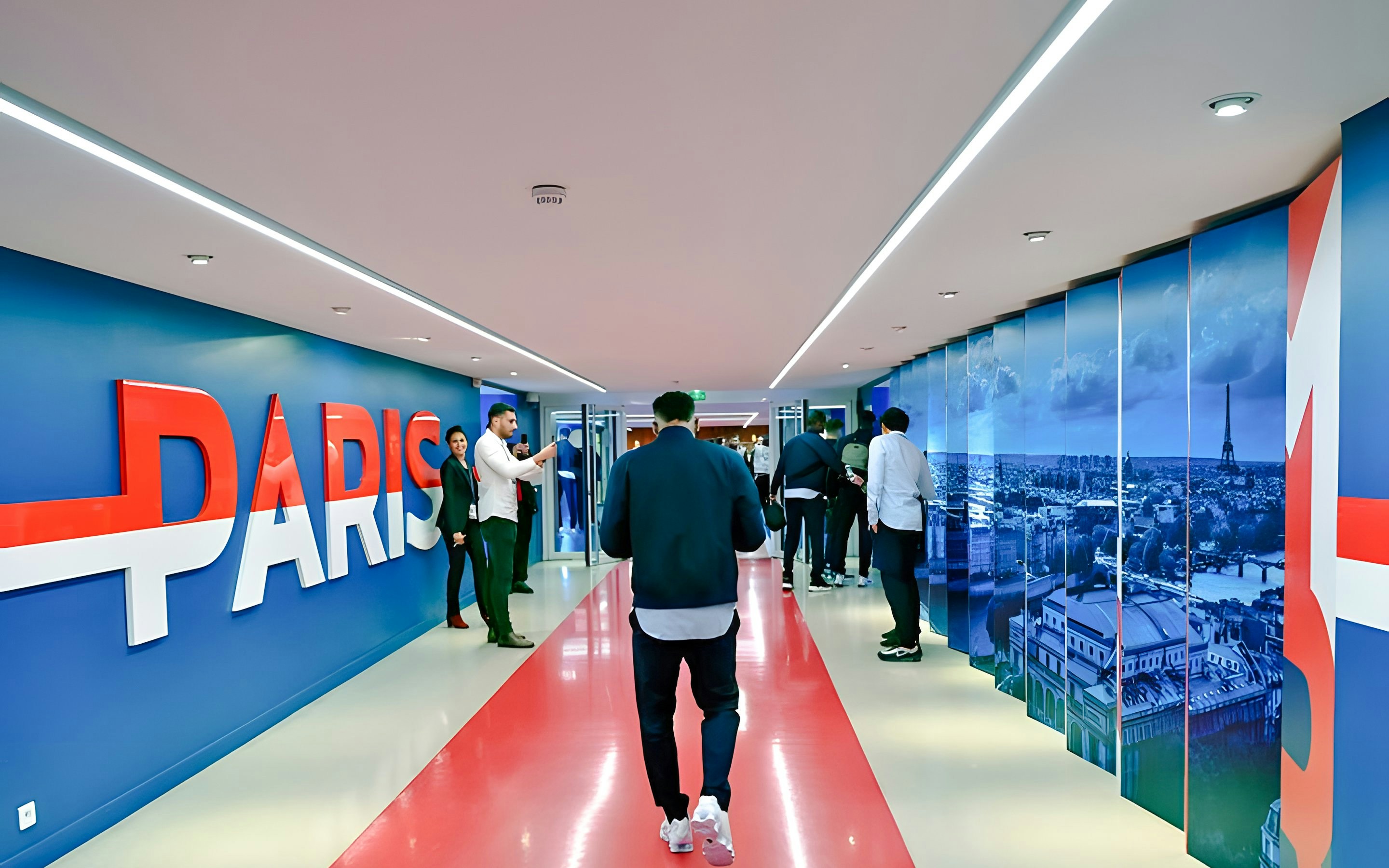 Hallway inside PSG Stadium, Paris, with people walking and large "Paris" sign on the wall.