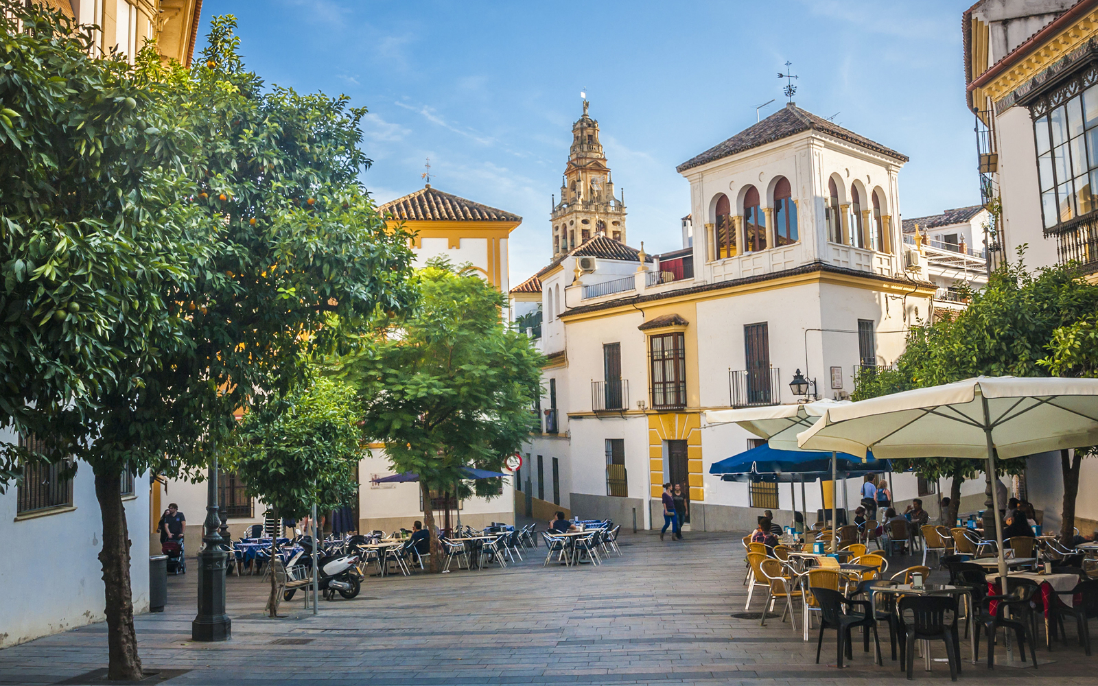 Cordoba street view with outdoor cafes and Mosque-Cathedral tower in background.