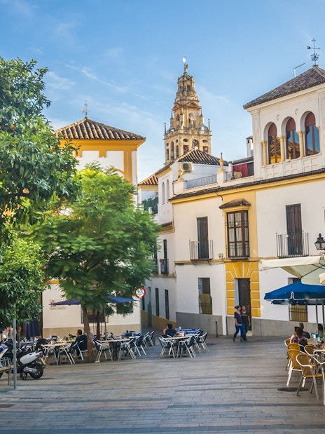 Cordoba street view with outdoor cafes and Mosque-Cathedral tower in background.