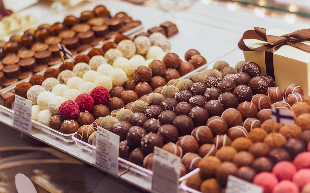 Assorted chocolates on display in a chocolate shop with a gift box in the background.
