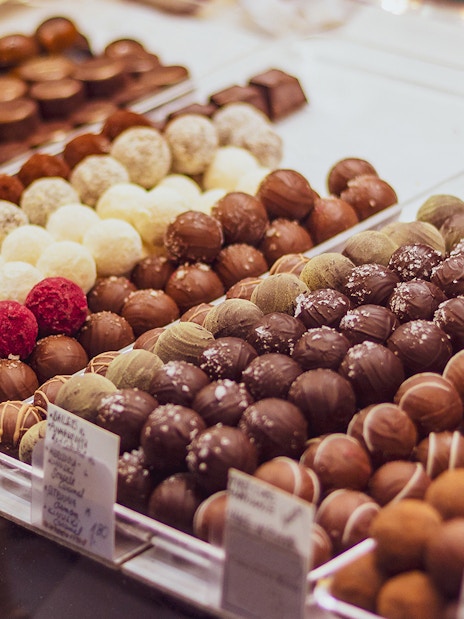 Assorted chocolates on display in a chocolate shop with a gift box in the background.