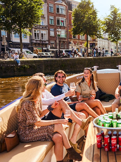 Guests enjoying drinks on a luxury canal cruise in Amsterdam with cityscape views.