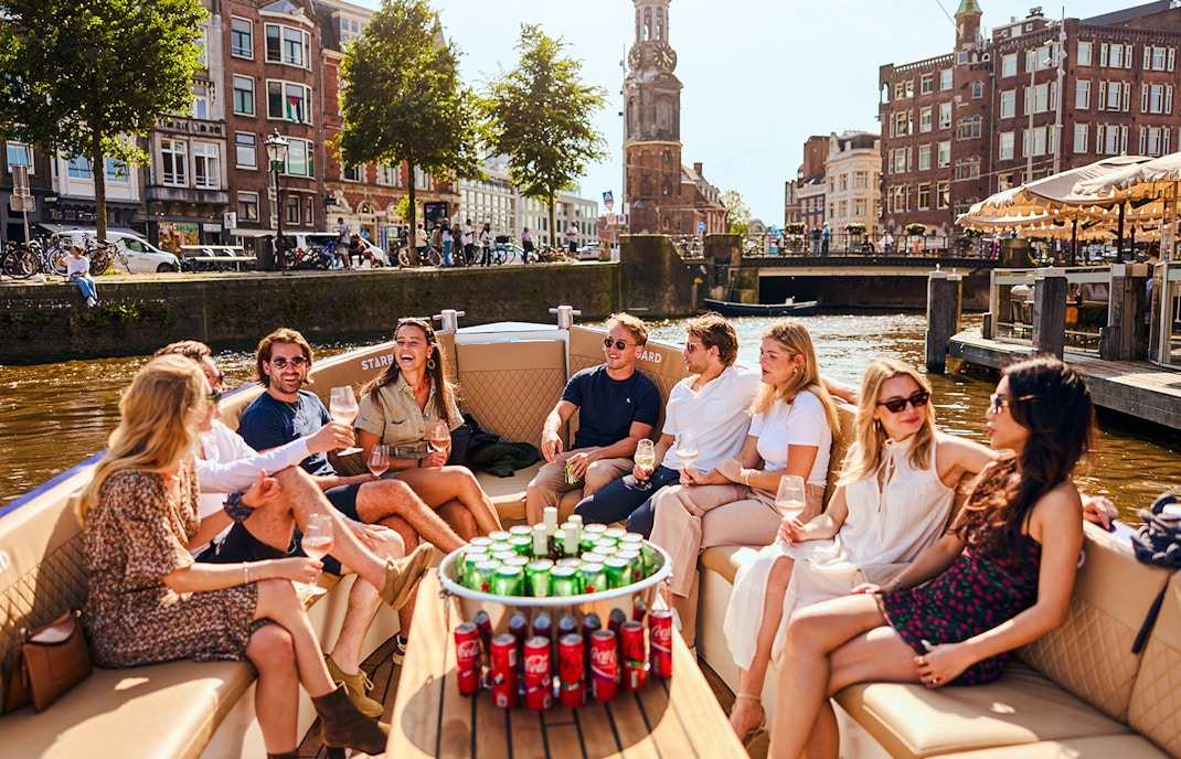 Guests enjoying drinks on a luxury canal cruise in Amsterdam with cityscape views.
