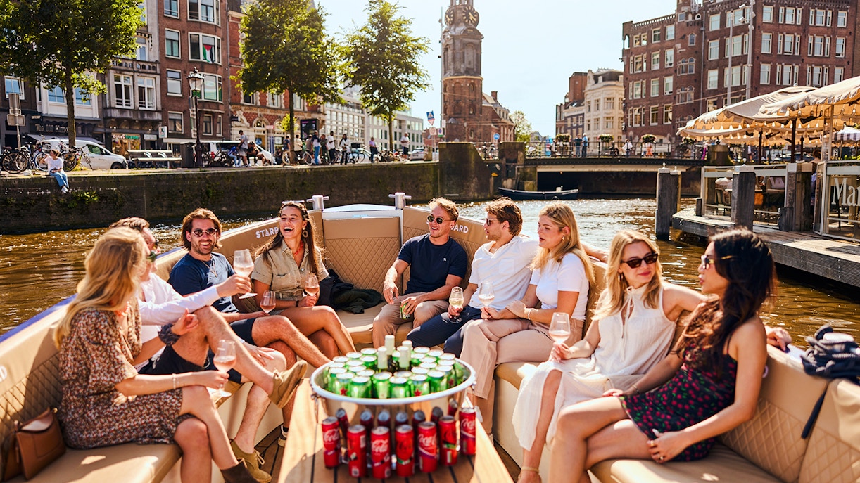 Guests enjoying drinks on a luxury canal cruise in Amsterdam with cityscape views.