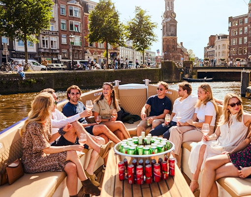 Guests enjoying drinks on a luxury canal cruise in Amsterdam with cityscape views.