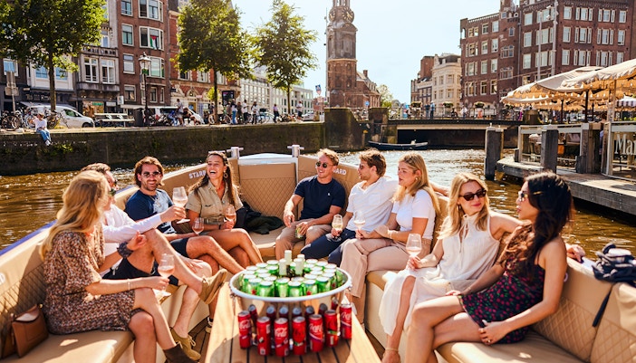 Guests enjoying drinks on a luxury canal cruise in Amsterdam with cityscape views.