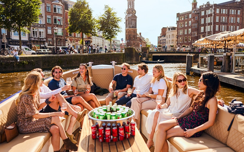 Guests enjoying drinks on a luxury canal cruise in Amsterdam with cityscape views.