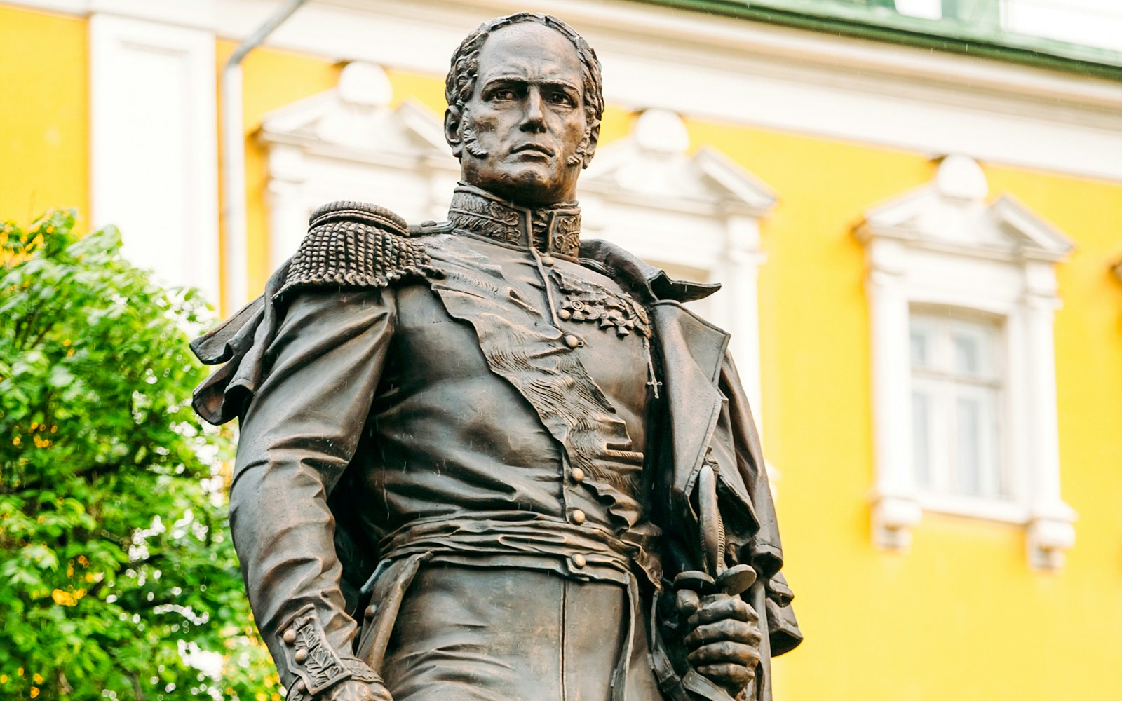 Statue of Emperor Alexander I in front of a yellow building.