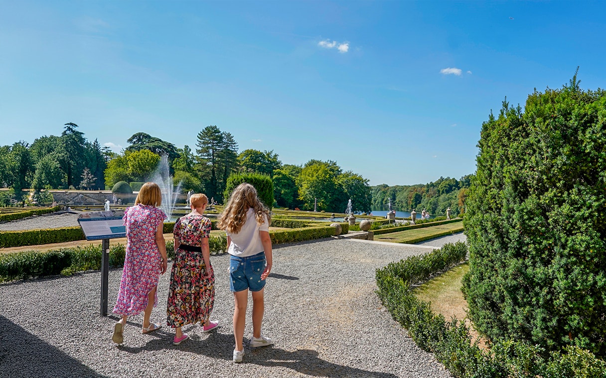 Visitors walking through palace gardens with fountains and manicured hedges.