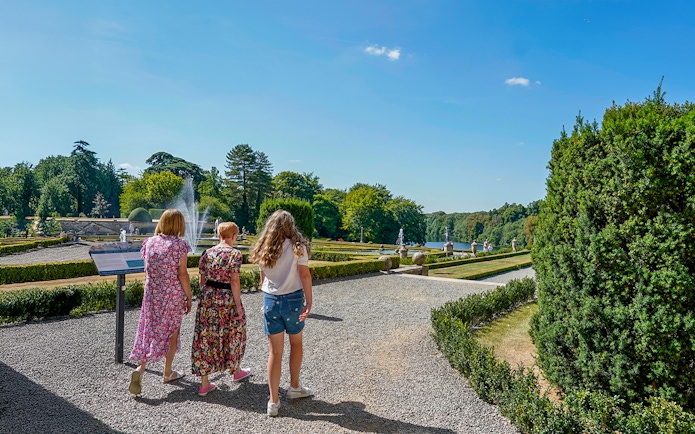 Visitors walking through palace gardens with fountains and manicured hedges.