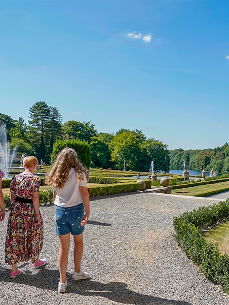Visitors walking through palace gardens with fountains and manicured hedges.