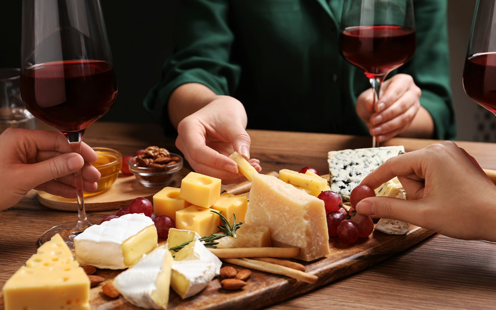 Cheese platter with assorted cheeses, grapes, and red wine glasses during a tasting event.