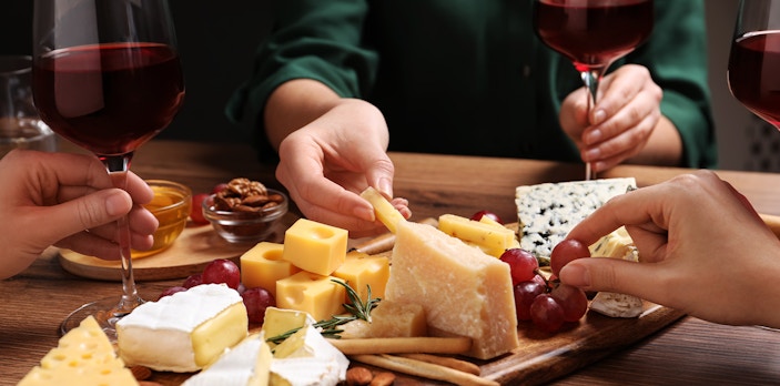 Cheese platter with assorted cheeses, grapes, and red wine glasses during a tasting event.