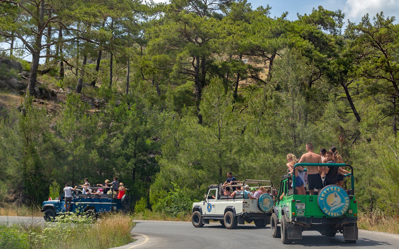 Jeeps with tourists driving through forested area in Antalya during guided safari tour.
