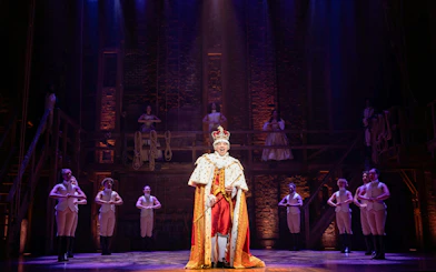 Hamilton West End performance with actor in royal costume on stage.