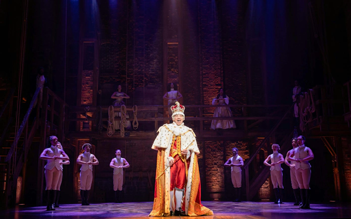 Hamilton West End performance with actor in royal costume on stage.