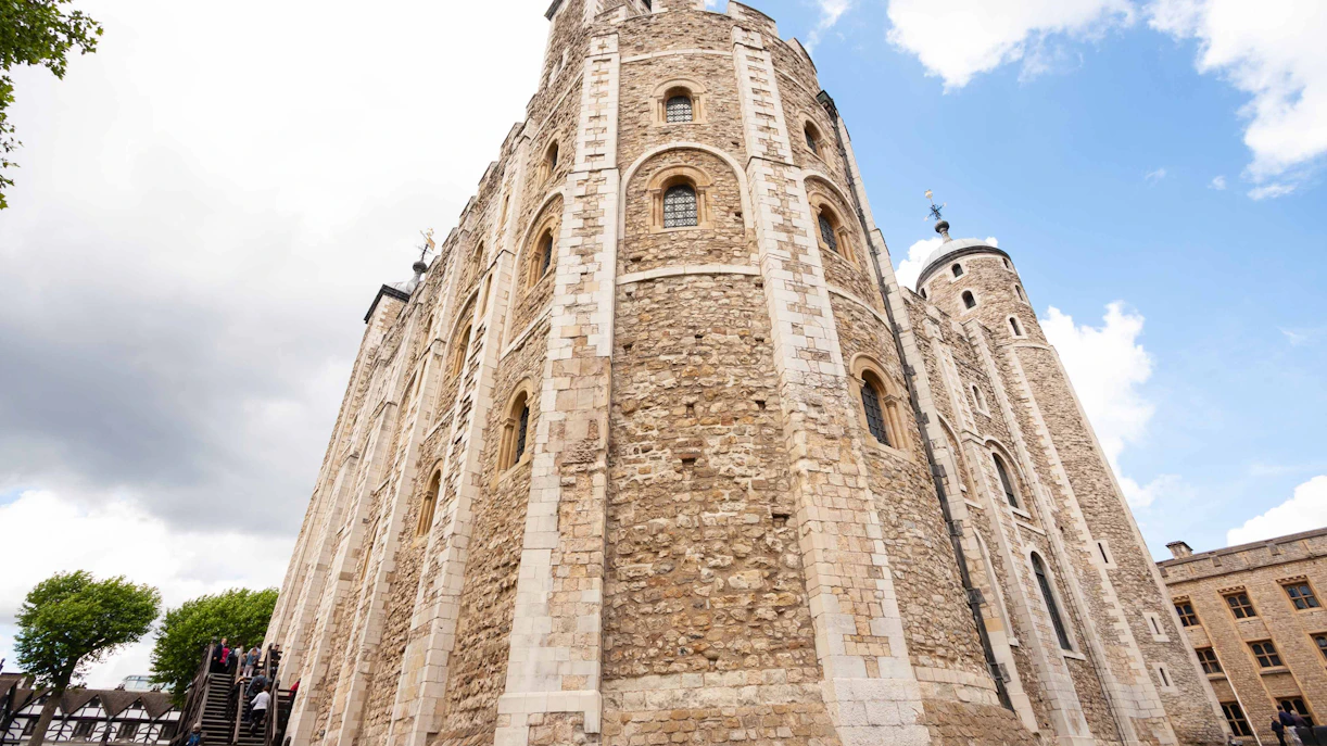Tower of London stone walls with visitors ascending wooden stairs.