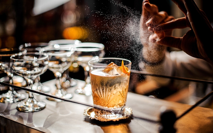 Bartender adding garnish to an old fashioned cocktail on a bar counter.