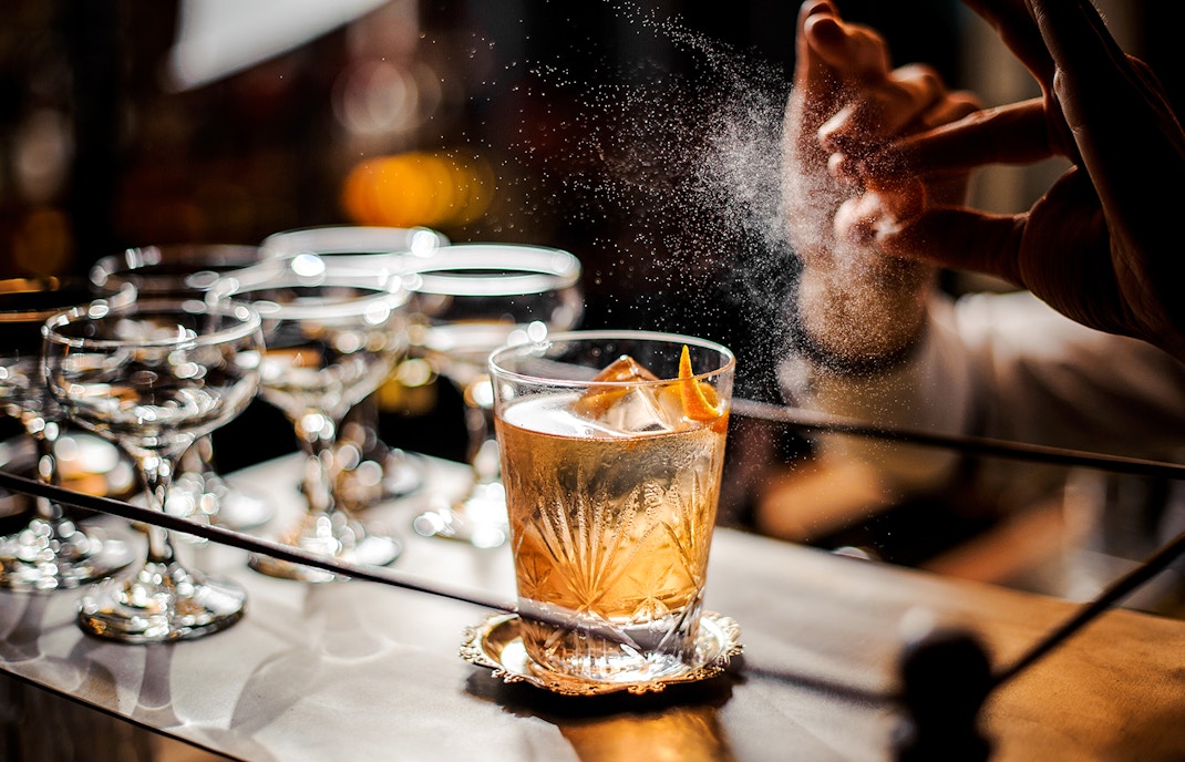 Bartender adding garnish to an old fashioned cocktail on a bar counter.