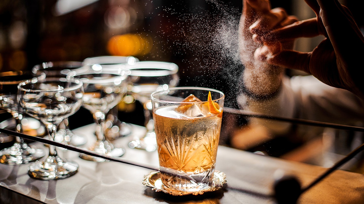 Bartender adding garnish to an old fashioned cocktail on a bar counter.