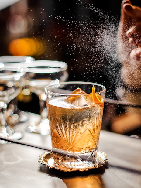 Bartender adding garnish to an old fashioned cocktail on a bar counter.