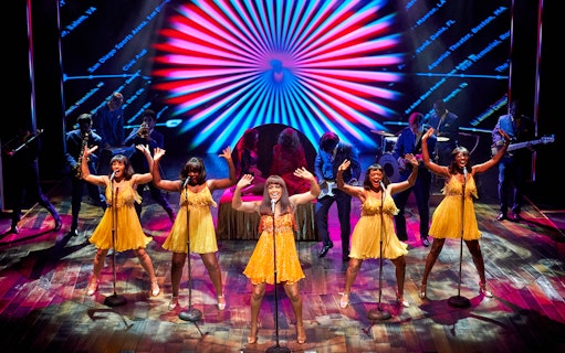 Performers in yellow dresses singing on stage during TINA: The Tina Turner Musical.
