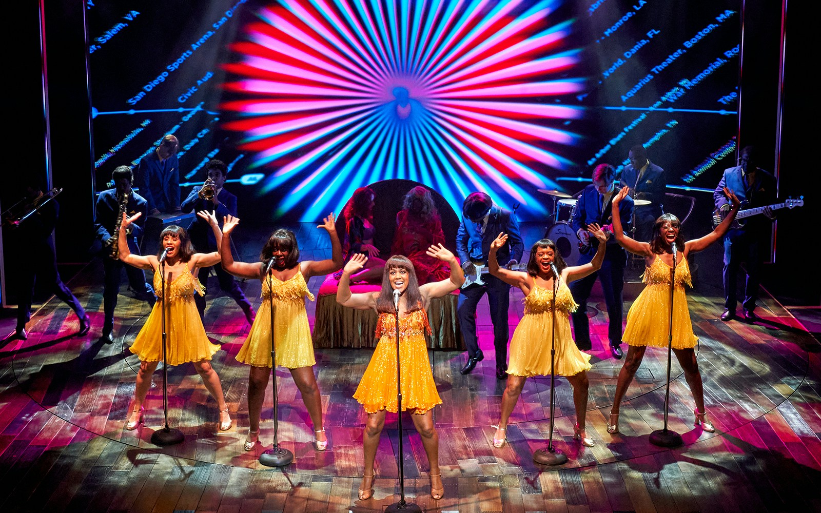 Performers in yellow dresses singing on stage during TINA: The Tina Turner Musical.
